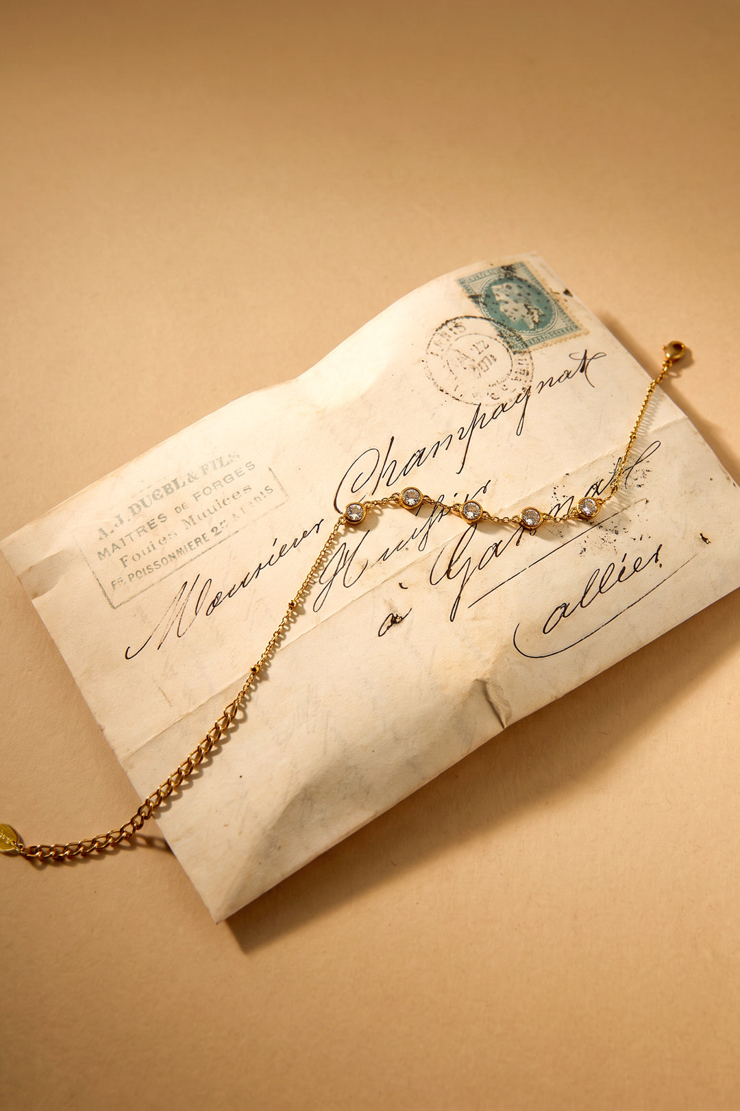 Gold geometric charm bracelet with clear stones on an antique envelope.
