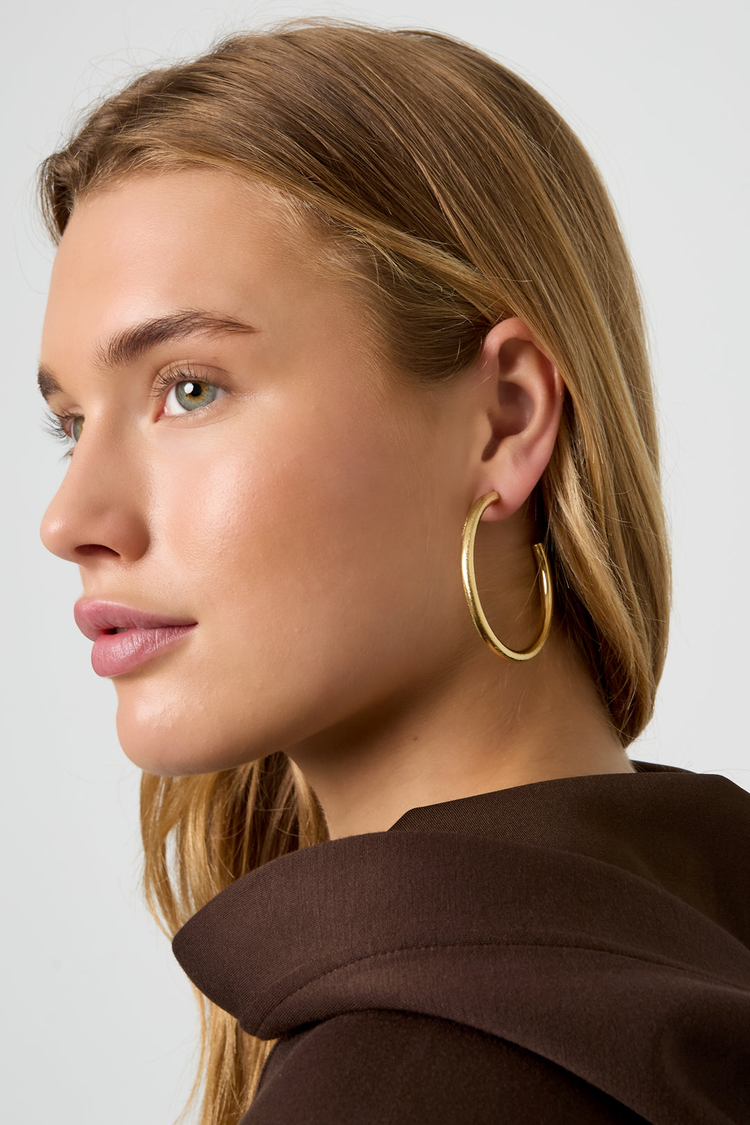 Astra Hoop Earrings: Gold-plated 18K gold PVD steel hoops on a woman's ear.