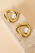 Gold circle stud earrings with a pearl accent, resting on a textured stone.