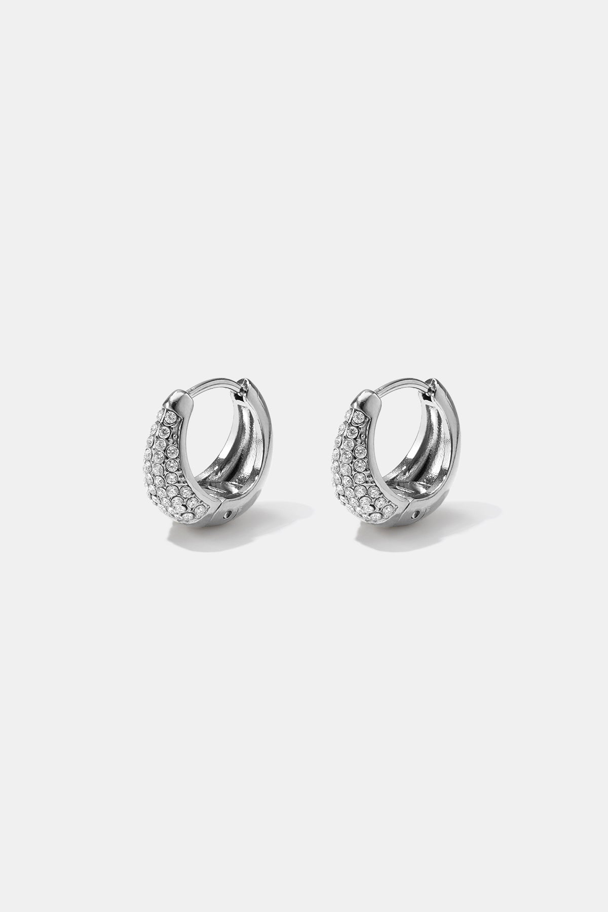 Silver hoop earrings with a curved design encrusted with small clear rhinestones.
