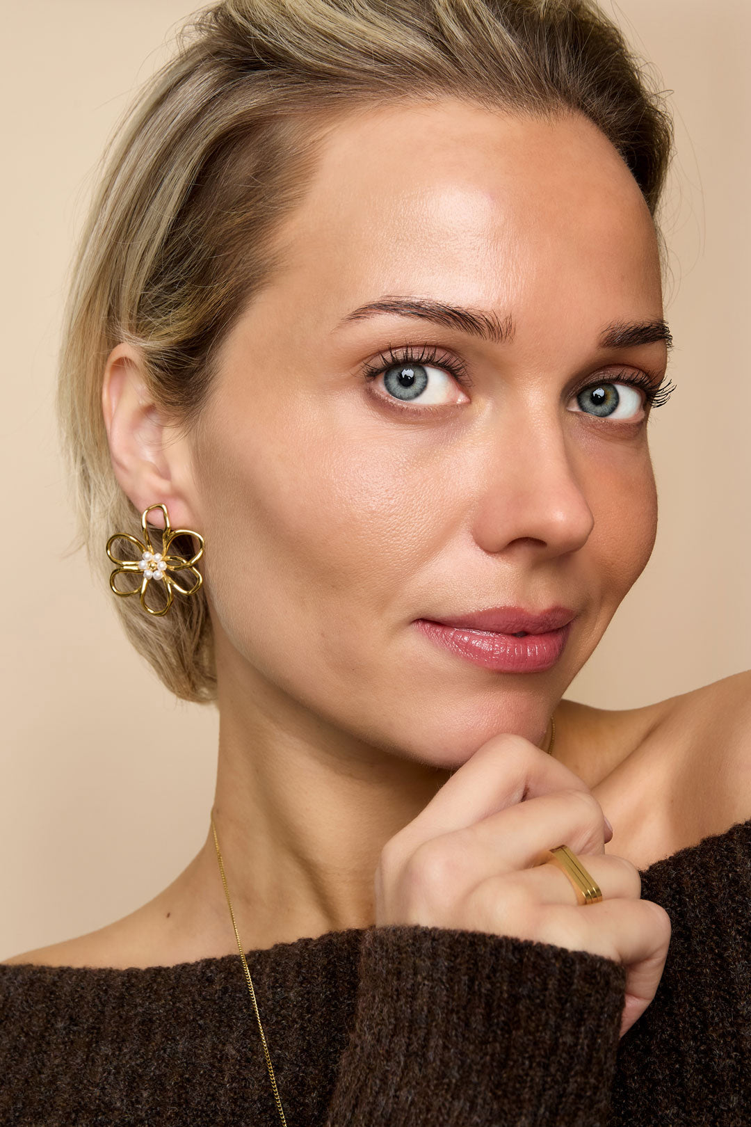Gold flower stud earrings with pearl accents, worn by a woman with blue eyes and blonde hair.