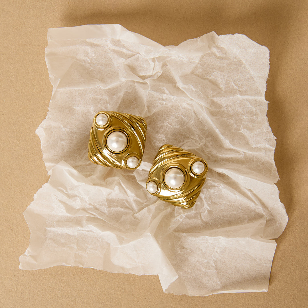 Aurelia stud earrings in gold with pearl accents on crumpled white paper.