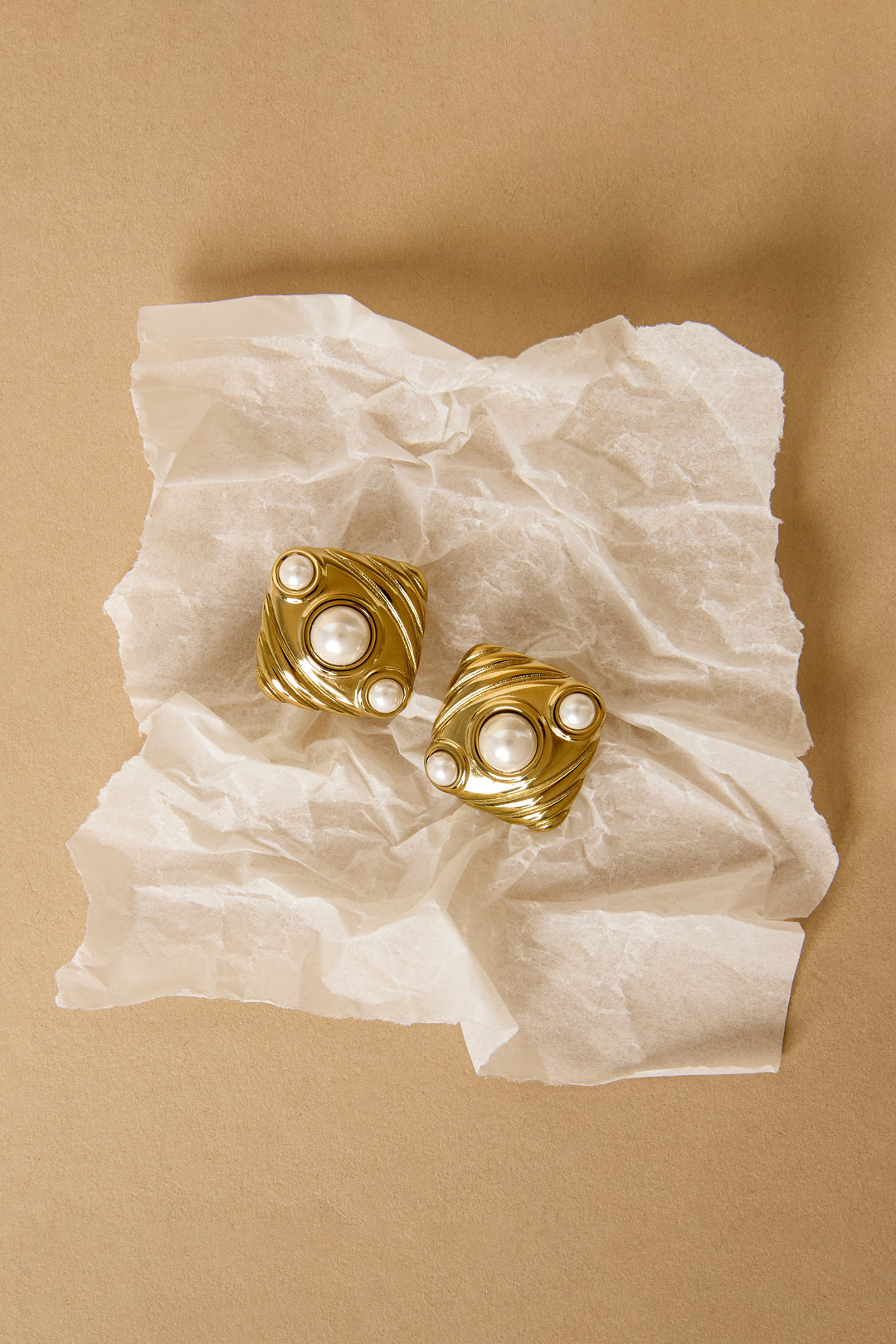 Aurelia stud earrings in gold with pearl accents on crumpled white paper.