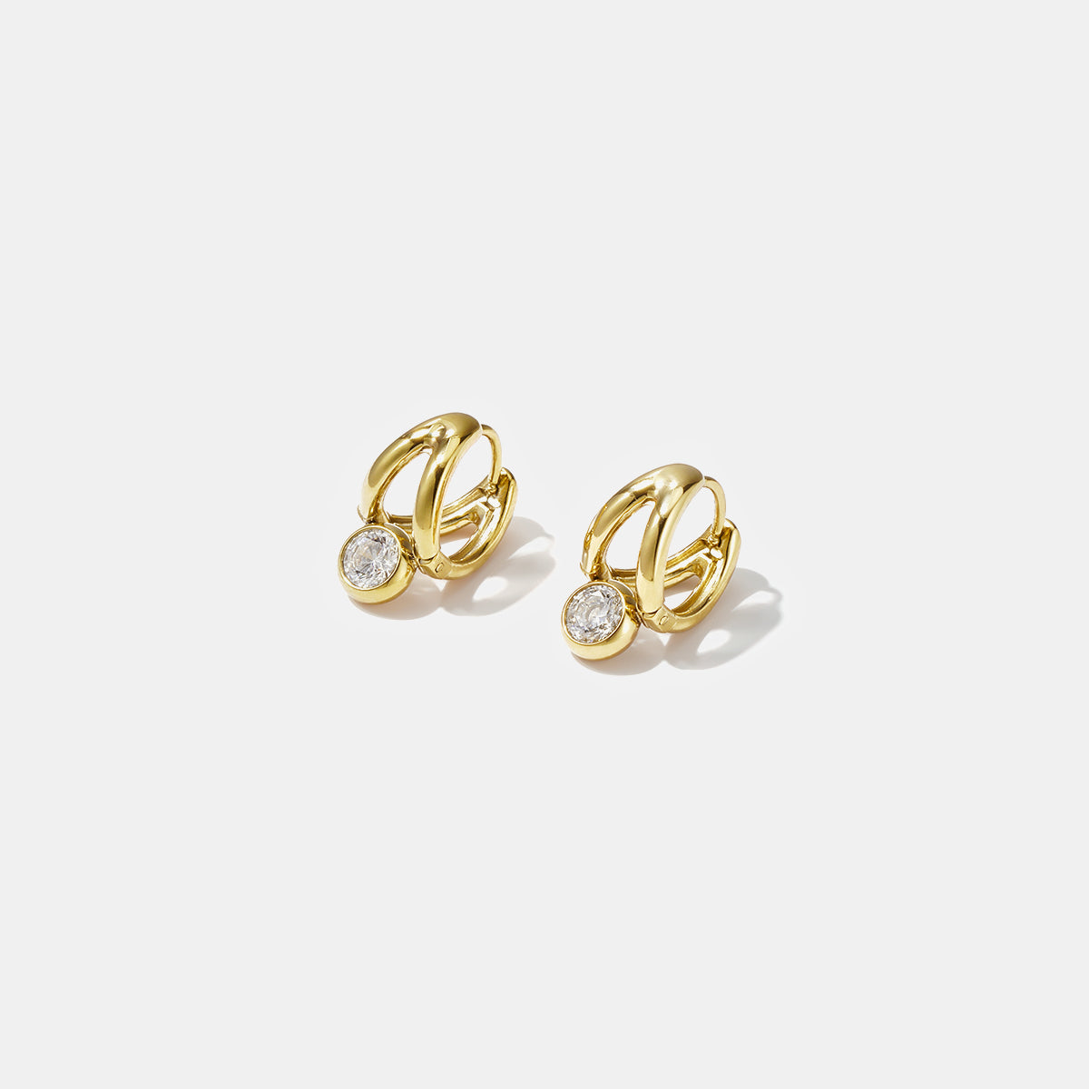 Gold irregular hoop earrings with a small clear stone hanging from each.