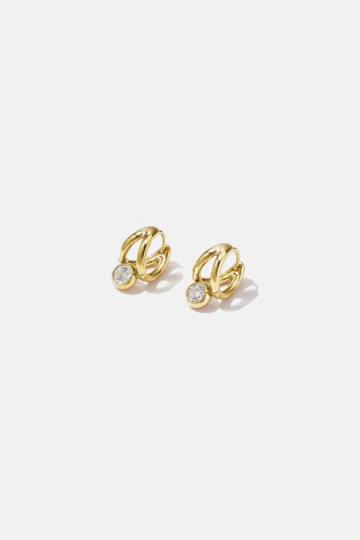 Gold irregular hoop earrings with a small clear stone hanging from each.