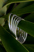 Silver Elara Bangle Bracelet with a brushed finish, 3 mm wide, resting on green leaves.