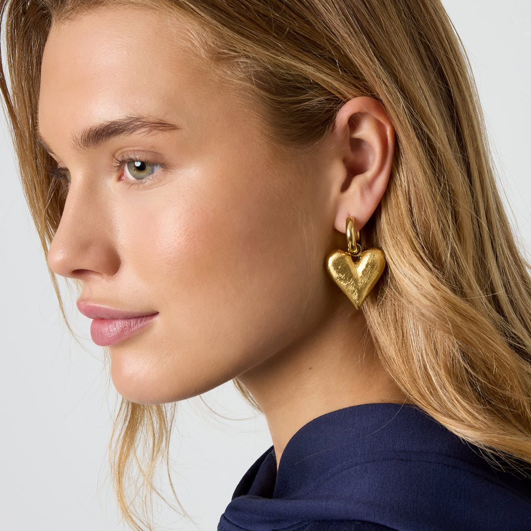 Gold heart drop earrings with a textured finish on a model.
