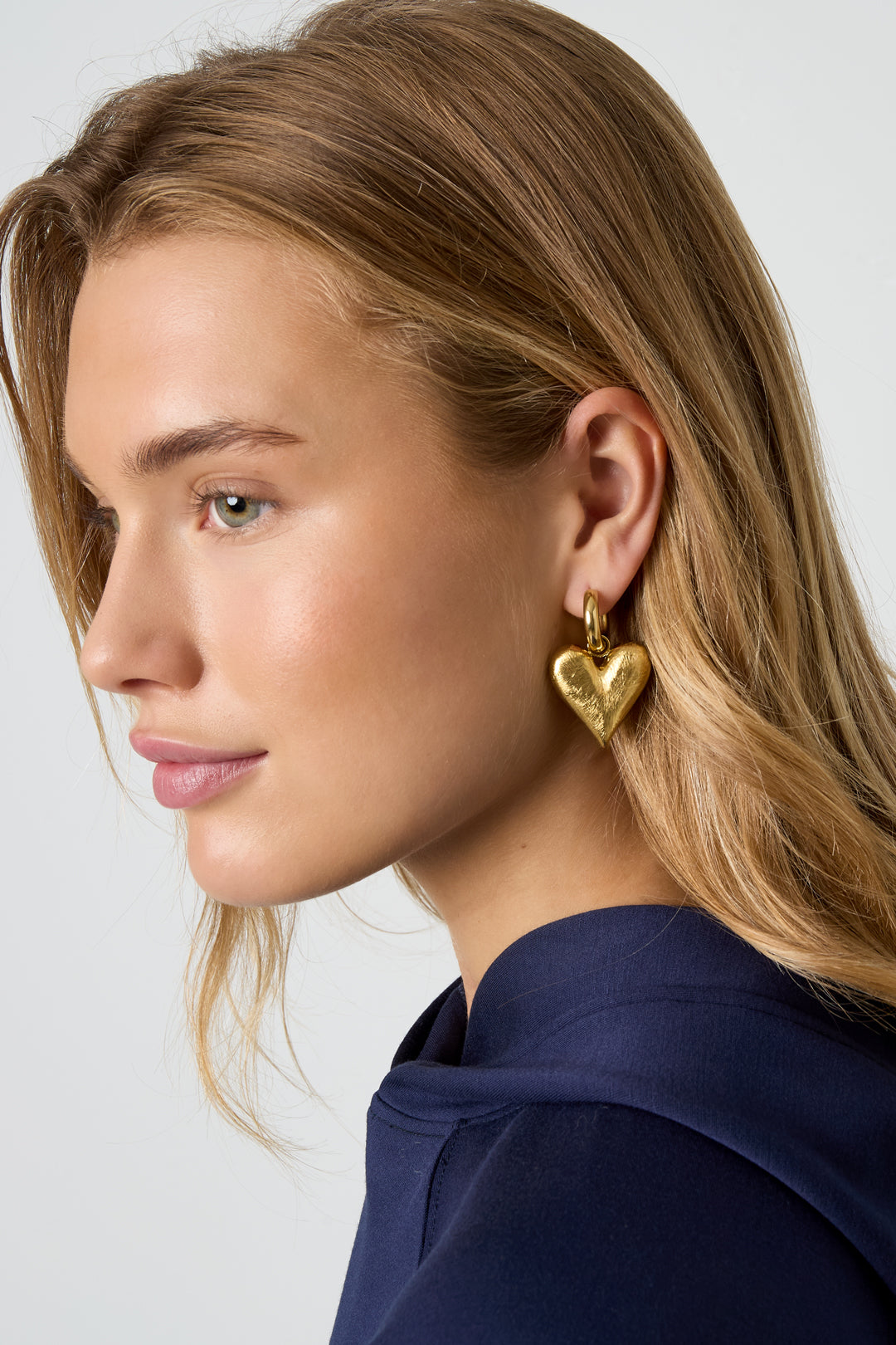 Gold heart drop earrings with a textured finish on a model.