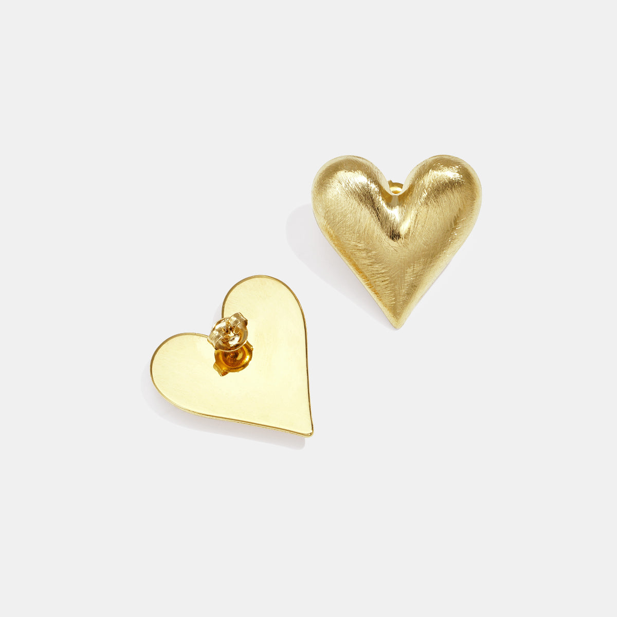 Gold heart stud earrings, one with a brushed finish, the other flat and smooth.
