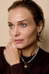 Gold heart drop earrings on a woman wearing a pearl necklace and a gold ring.