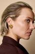 Gold-colored petal stud earrings with a textured surface, worn by a woman.