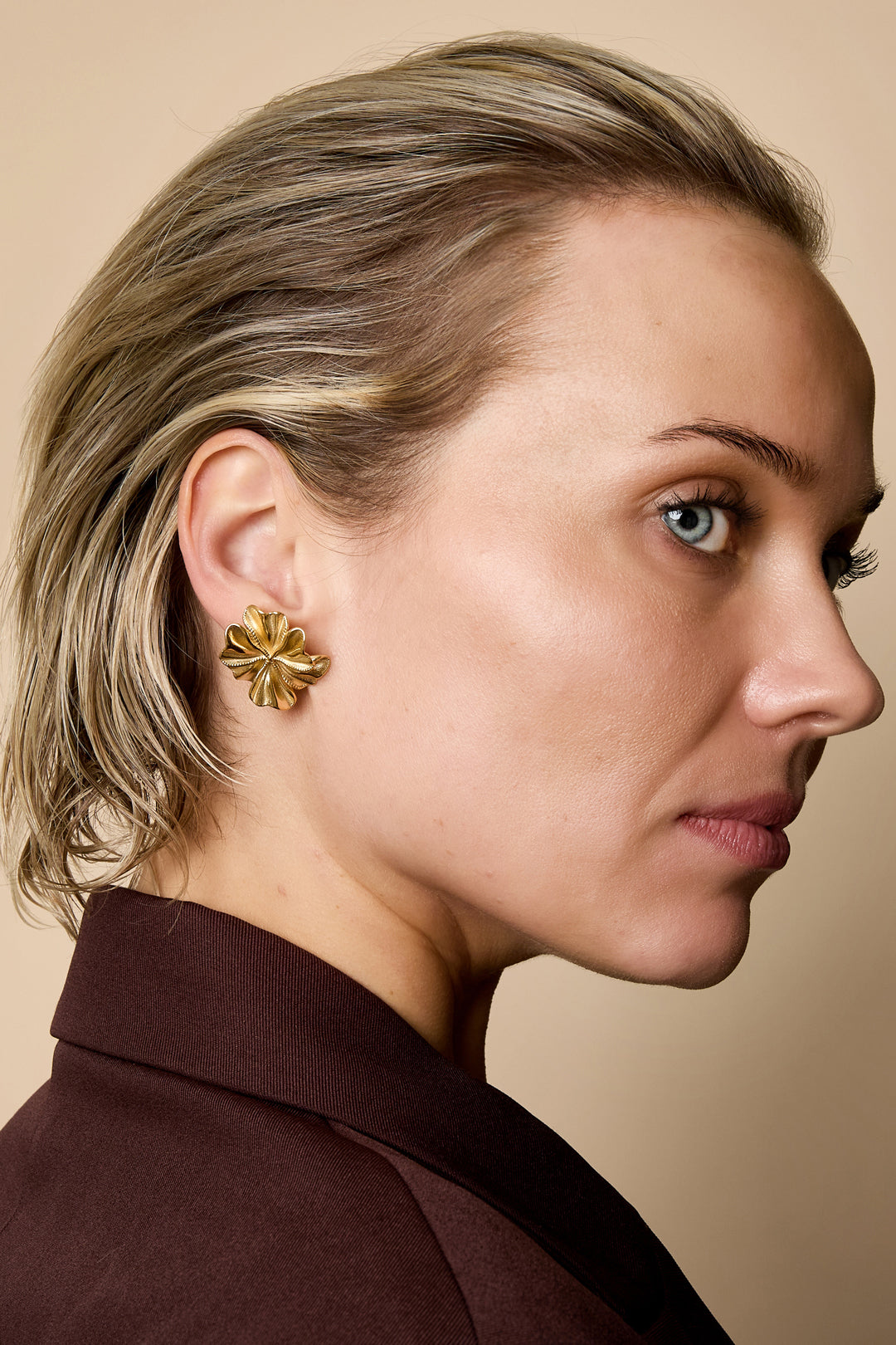 Gold-colored petal stud earrings with a textured surface, worn by a woman.
