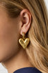 Gold heart drop earrings on a woman's ear.