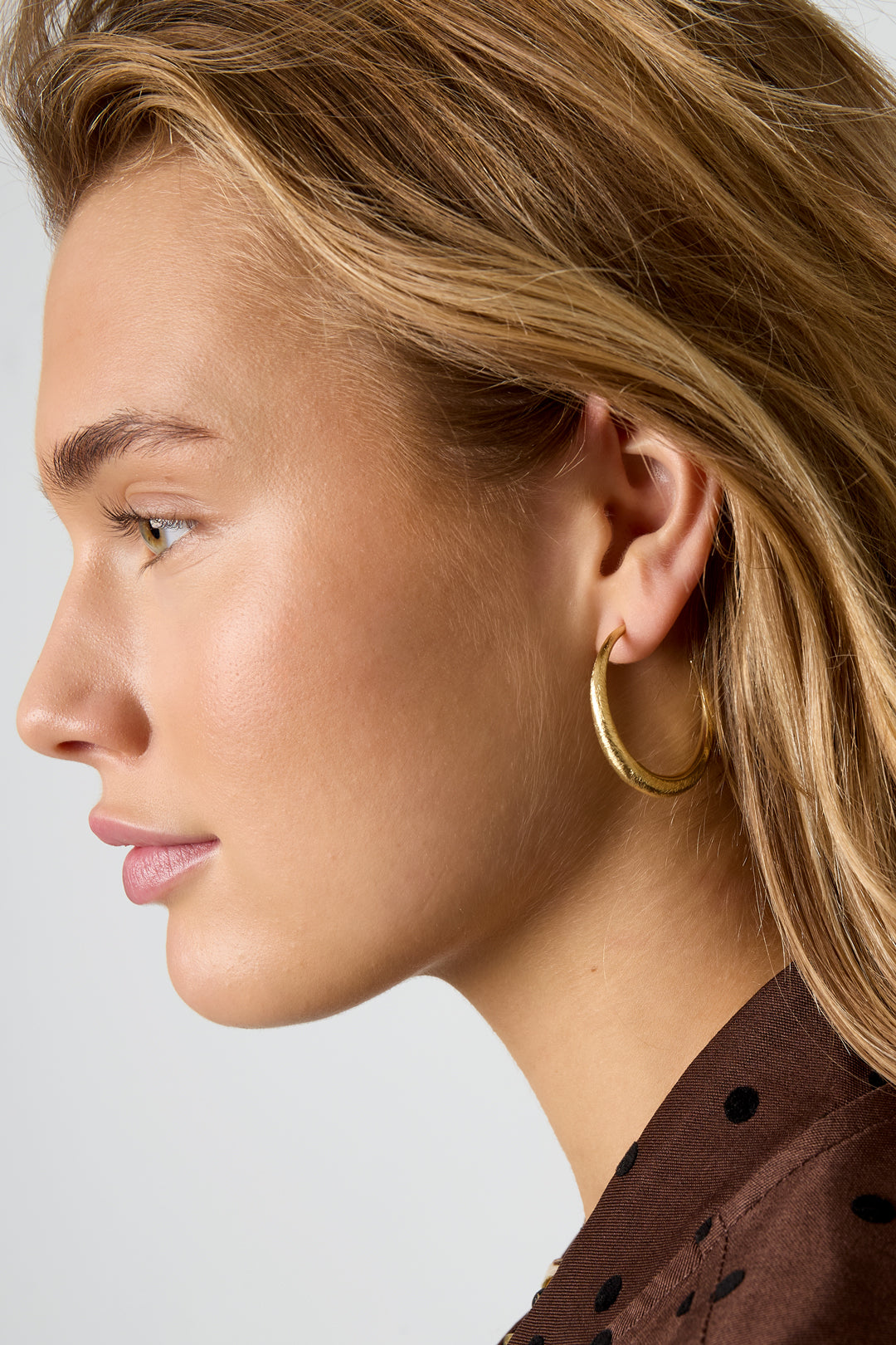 Gold Aurelia hoop earrings with a textured surface, worn by a woman.