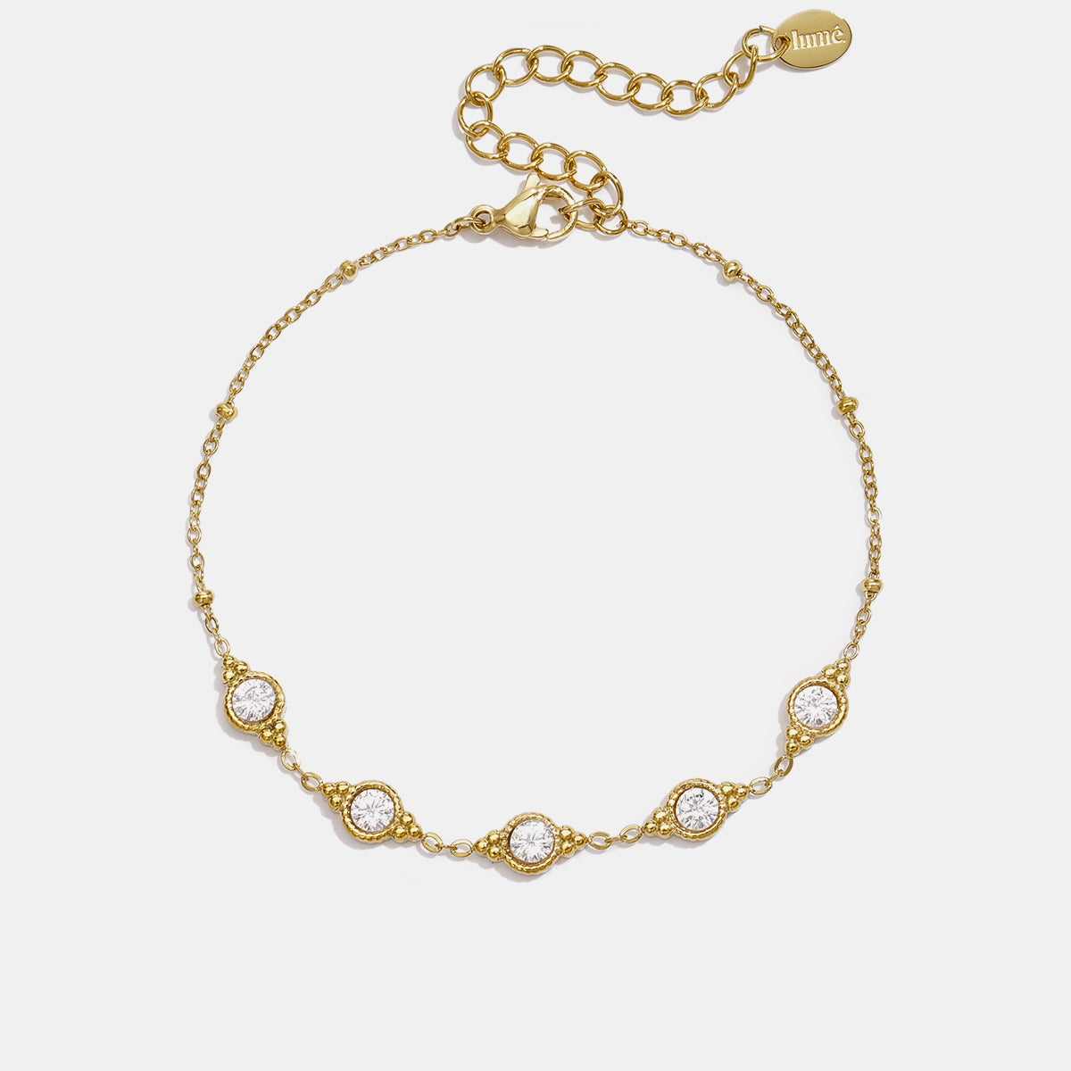 Gold geometric charm bracelet with five clear stones and beaded accents.