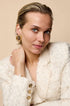 Gold-colored irregular hoop earrings on a woman with blue eyes and blonde hair.