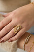 Gold ring with intertwined spiral design and a central zircon stone, worn on a finger.