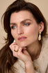 Woman wearing amber irregular earrings and a gold ring, with a beige fur coat.