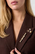 Gold-colored brooch with rhinestones in a droplet and heart design on a brown blazer.