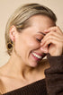 Gold-toned abstract bow-shaped earrings on a woman laughing.