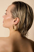 Gold-toned, irregular shaped hoop earrings on a woman's ear.
