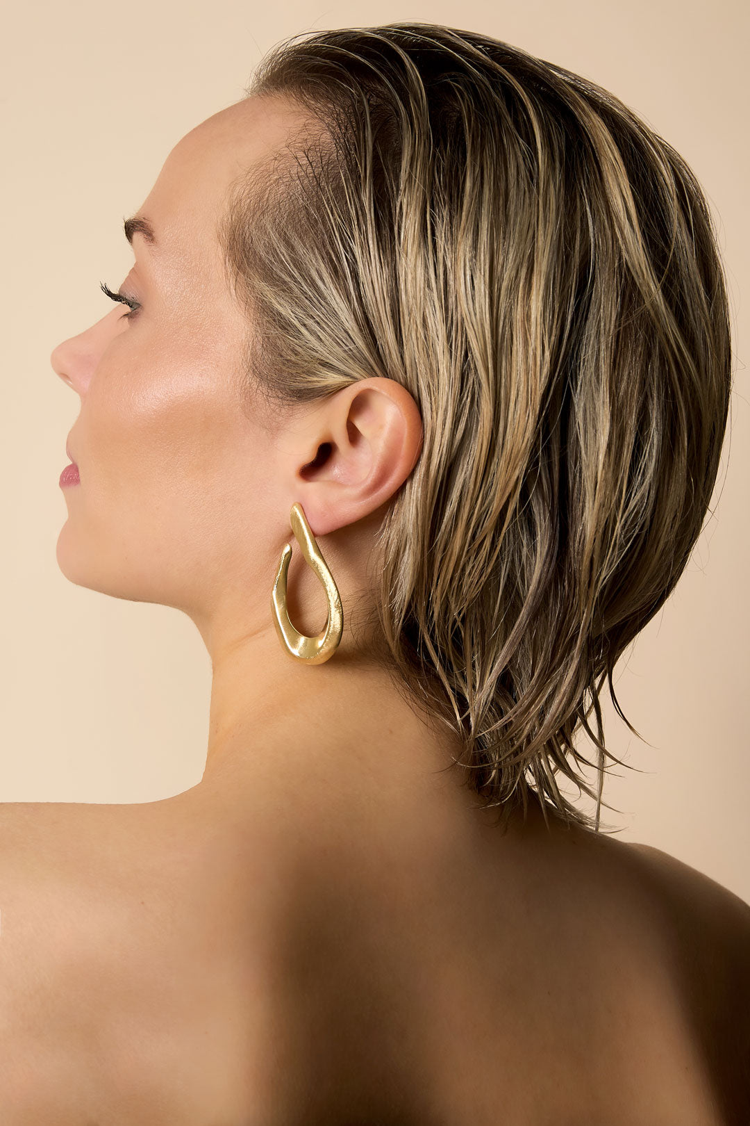 Gold-toned, irregular shaped hoop earrings on a woman's ear.