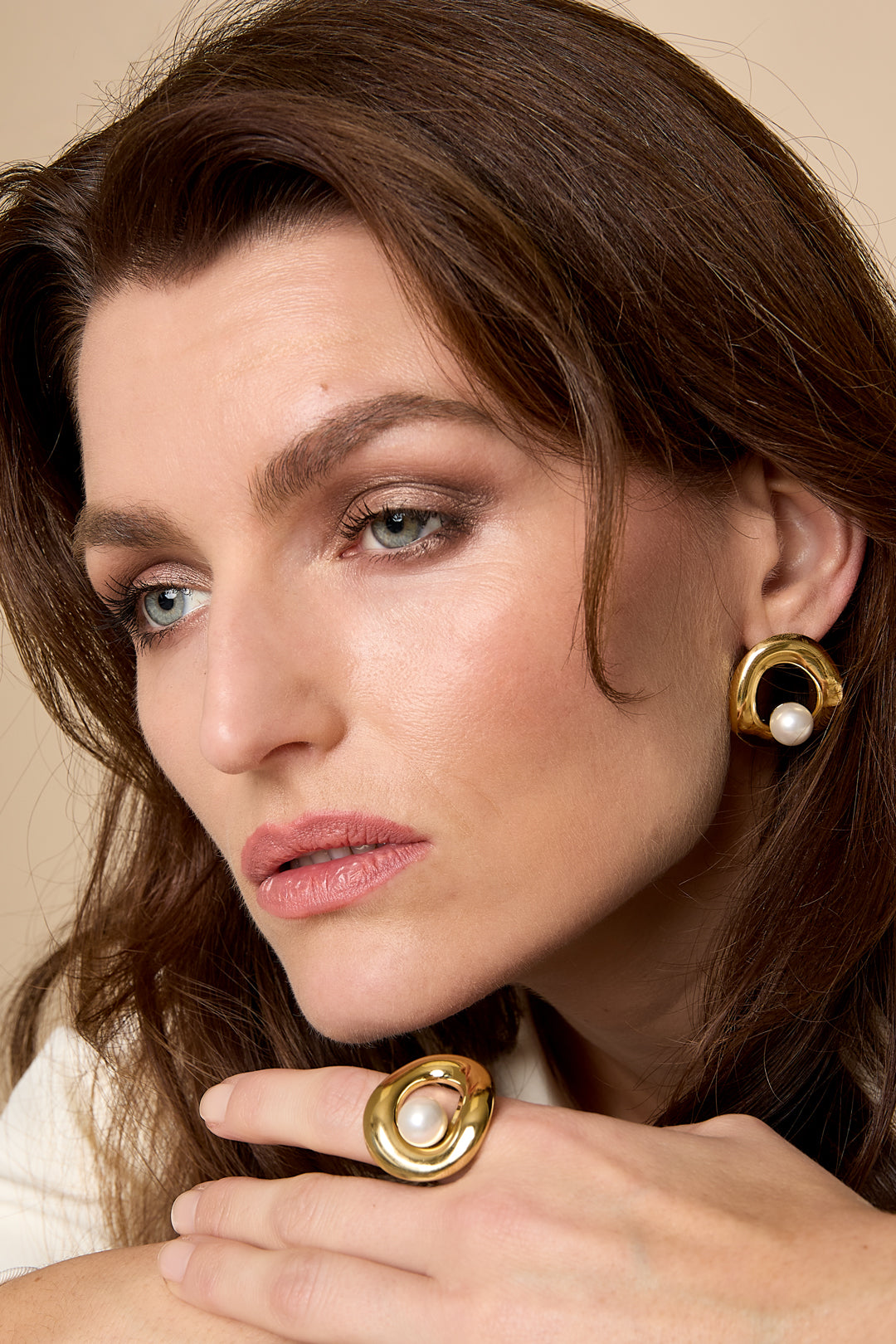 Gold circle stud earrings with a pearl accent, worn by a woman.
