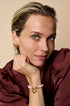 Gold heart stud earrings on a woman's ear, with a matching heart charm bracelet on her wrist.