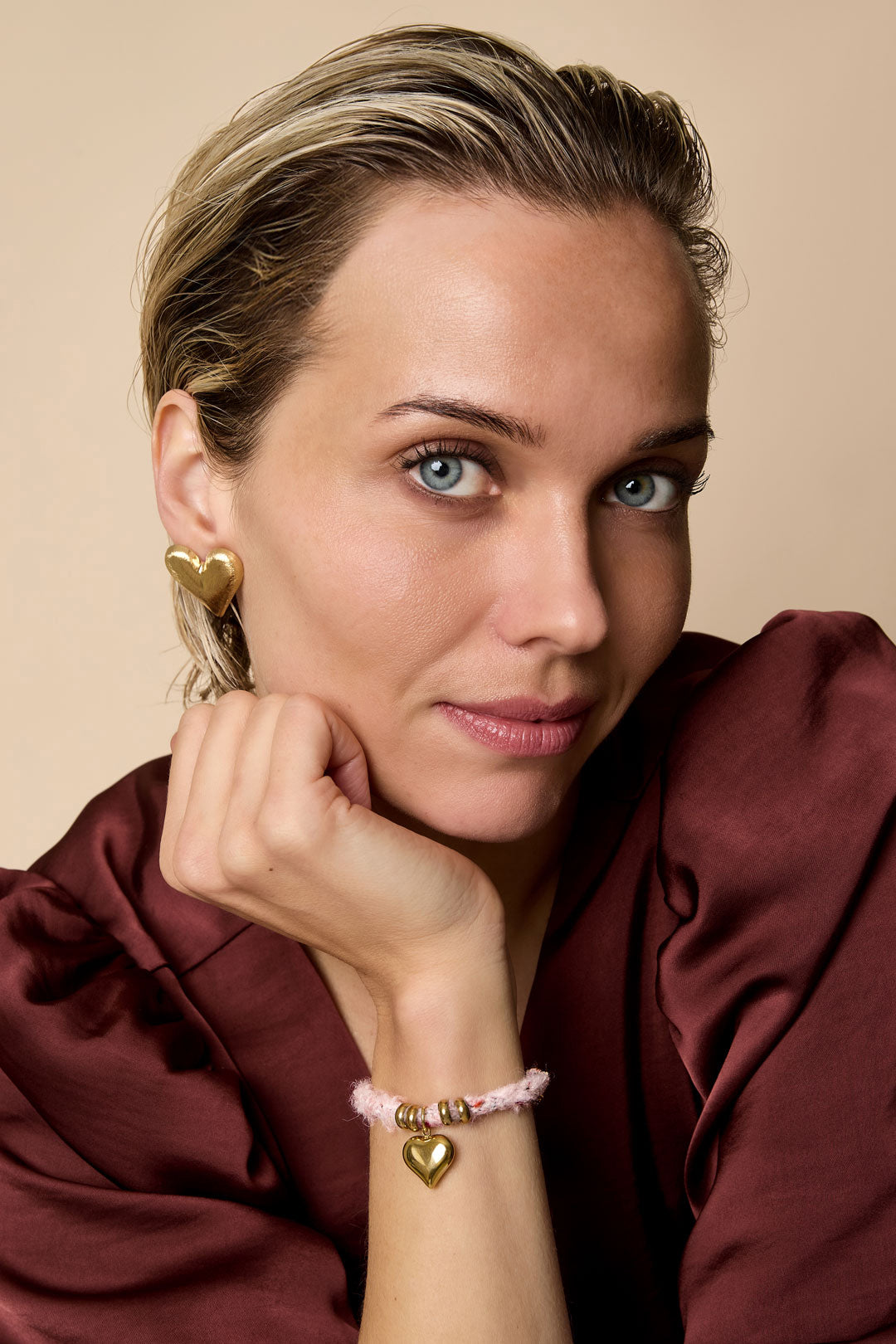 Gold heart stud earrings on a woman's ear, with a matching heart charm bracelet on her wrist.