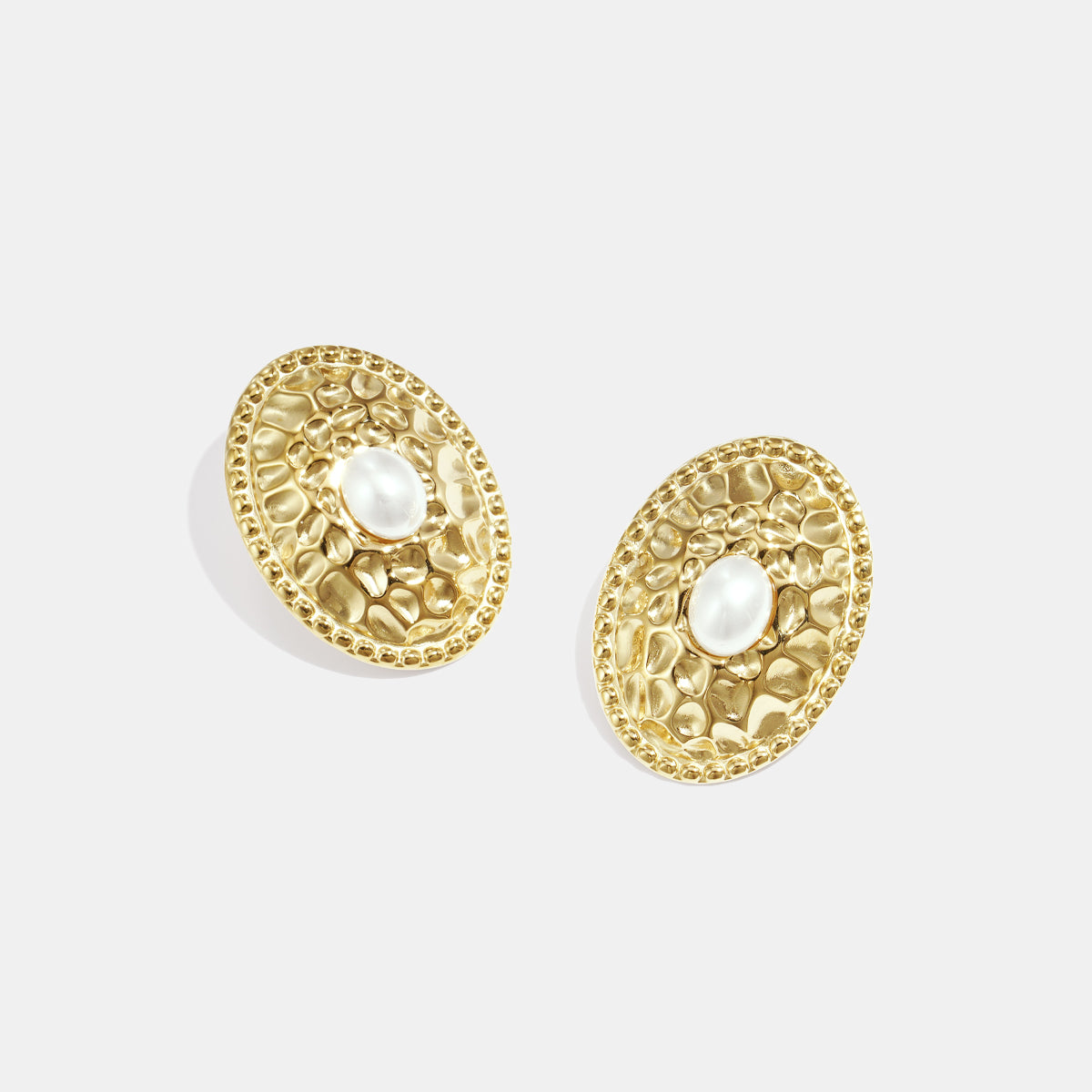Gold oval stud earrings with a hammered texture and a pearl in the center.