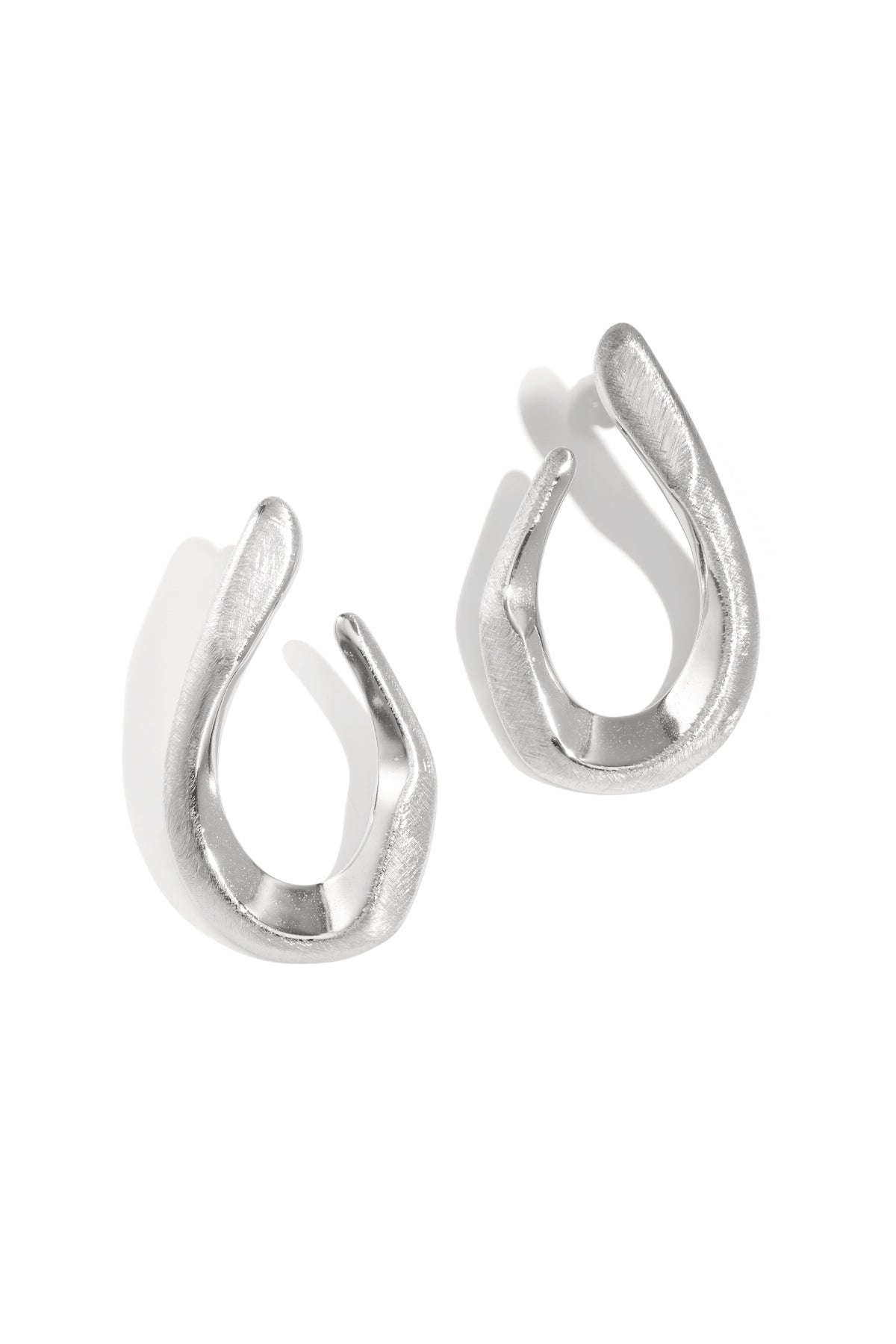 Two silver irregular shaped stud earrings with a brushed finish, casting shadows on a white background.