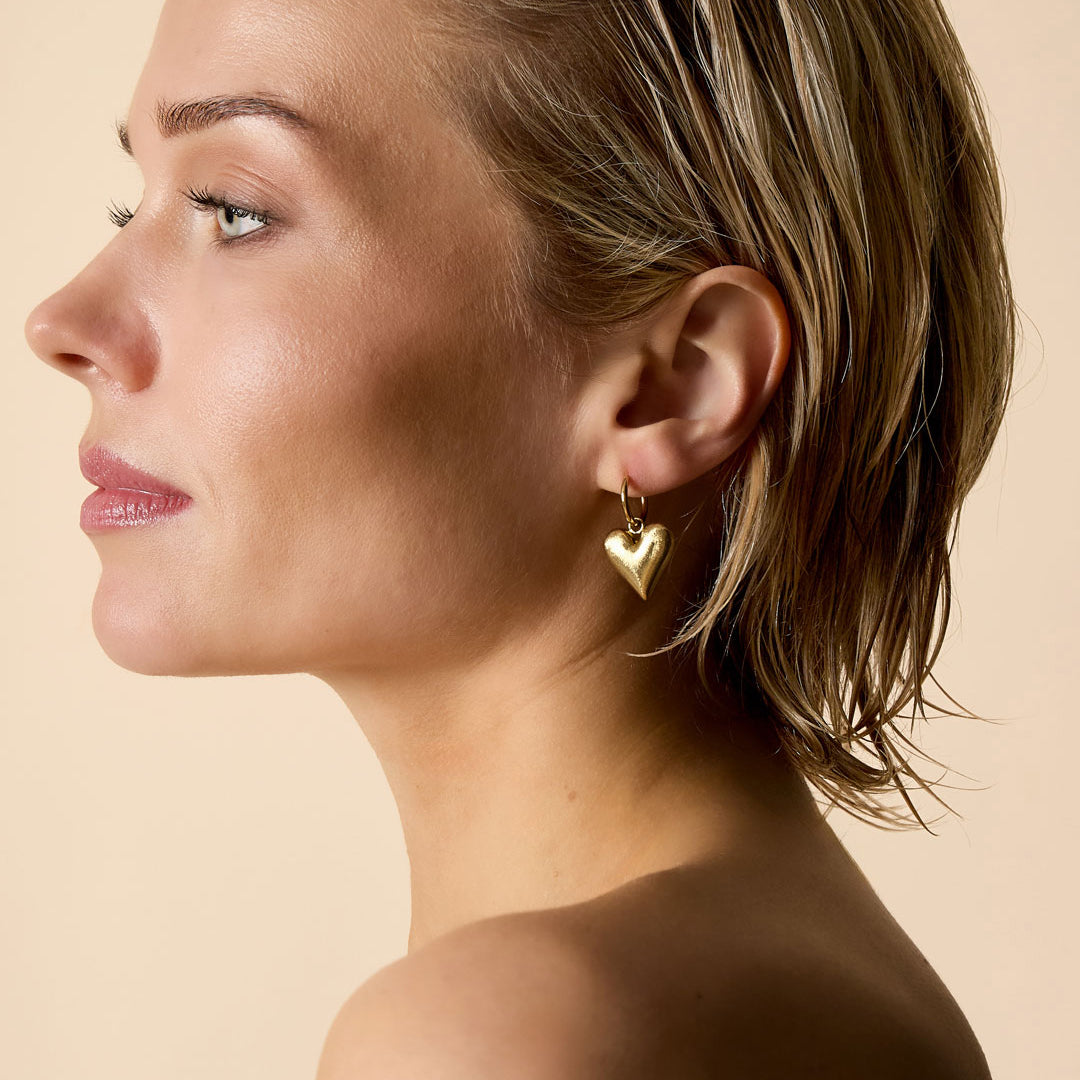 Gold heart drop earrings on a woman's ear.