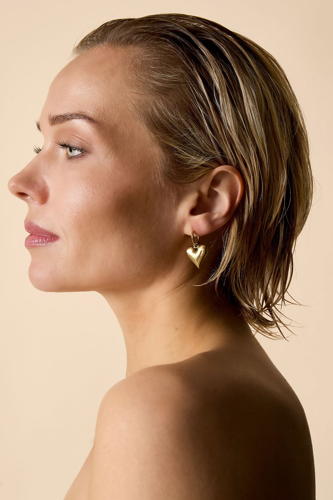 Gold heart drop earrings on a woman's ear.