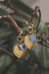 Gold hoop earrings with blue heart-shaped pendants hanging from a branch.