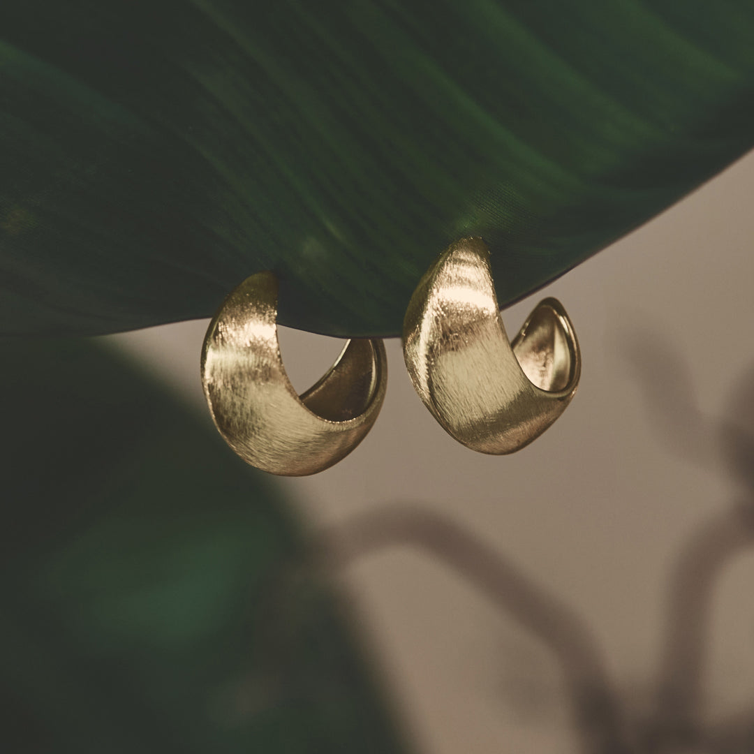 Aurelia Hoop Earrings in gold, shown on a green leaf.