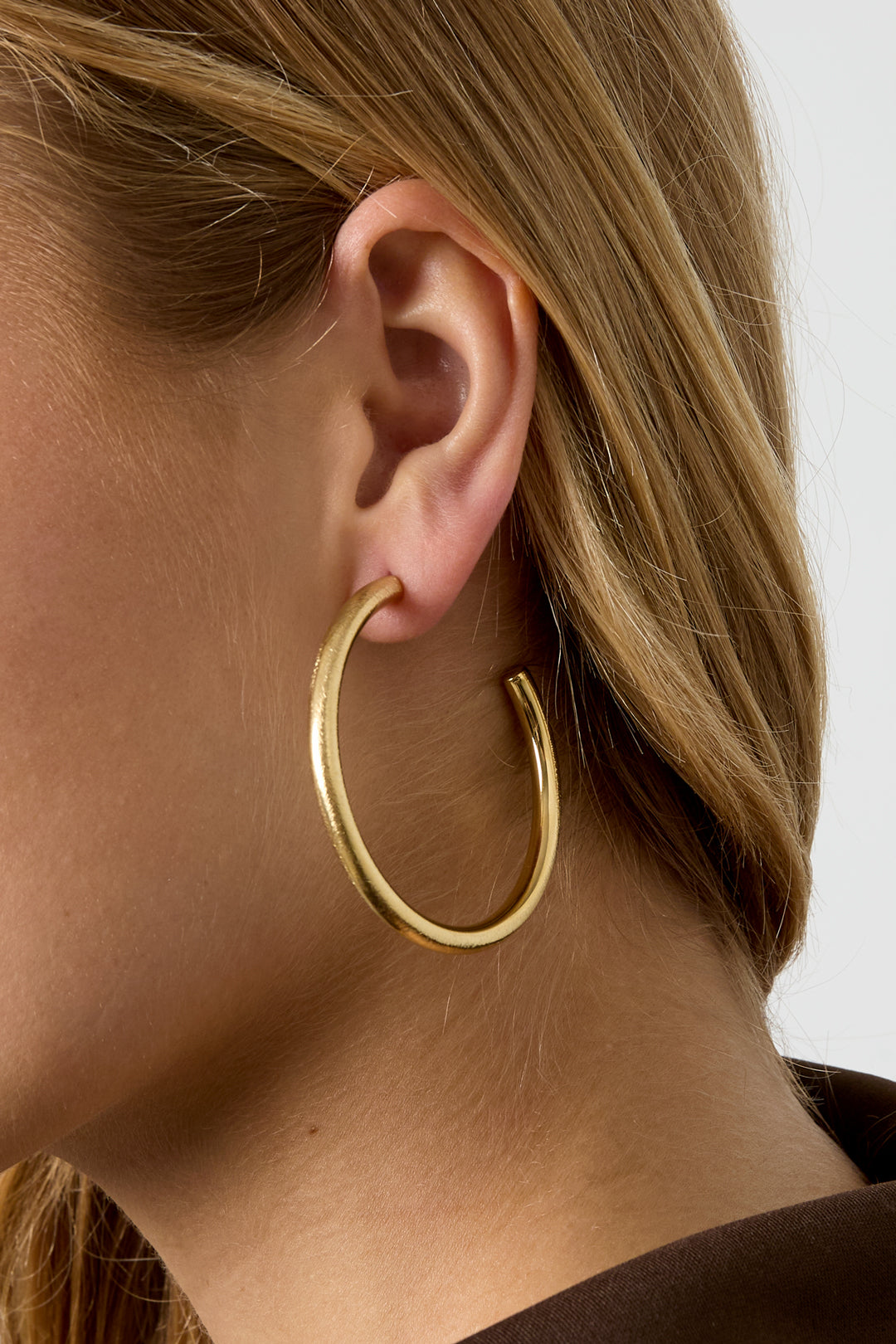 Gold hoop earrings with a brushed finish on a woman's ear.