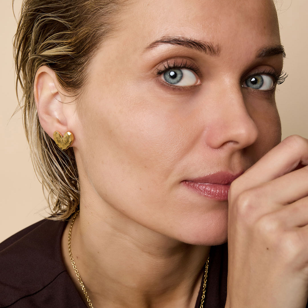 Gold heart-shaped stud earrings on a woman's ear.