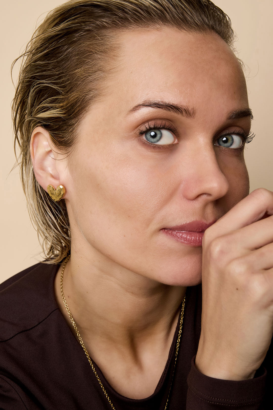 Gold heart-shaped stud earrings on a woman's ear.