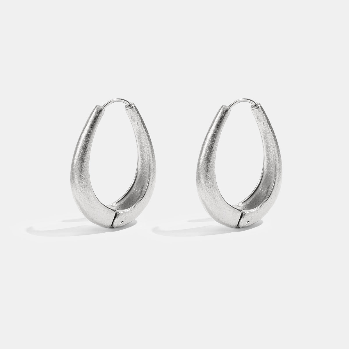 A pair of silver irregular oval hoop earrings with a brushed finish.