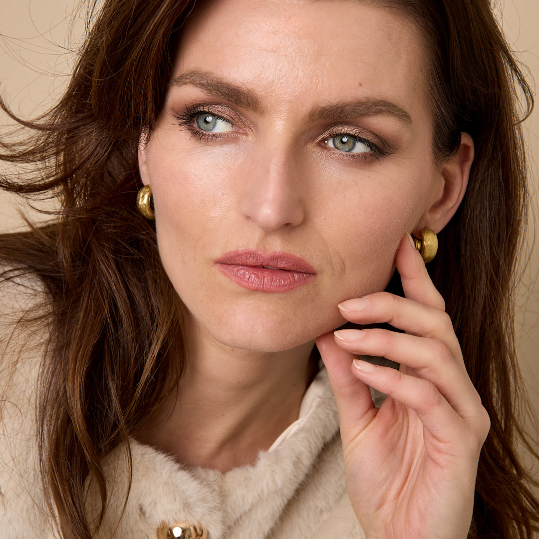 Elysian Hoop Earrings in gold, worn by a model with brown hair and light blue eyes.