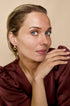 Gold irregular circle hoop earrings on a woman with blonde hair and blue eyes, wearing a maroon top.