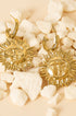 Gold sun drop earrings with detailed faces and rays, resting on white stones.