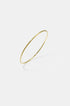 Thin gold bangle bracelet with a brushed finish, casting a shadow on a light grey background.