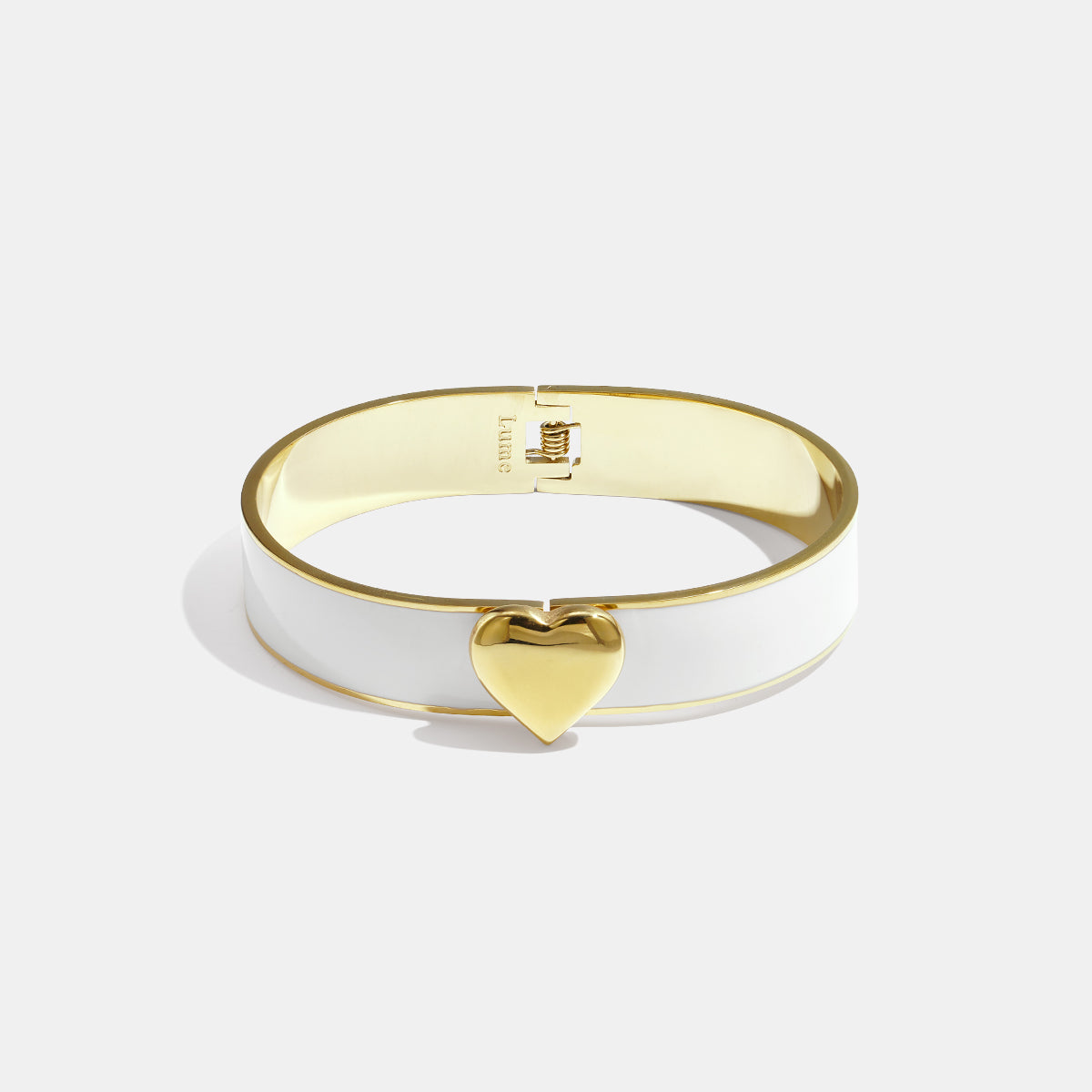 Gold heart charm on a white and gold bangle bracelet.