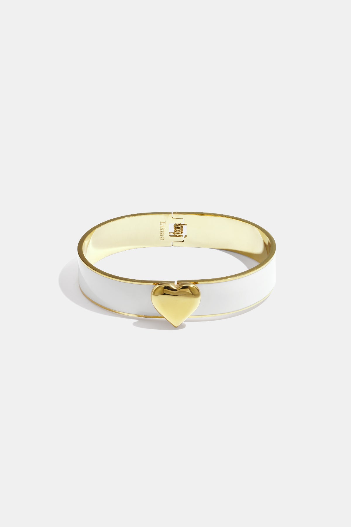 Gold heart charm on a white and gold bangle bracelet.