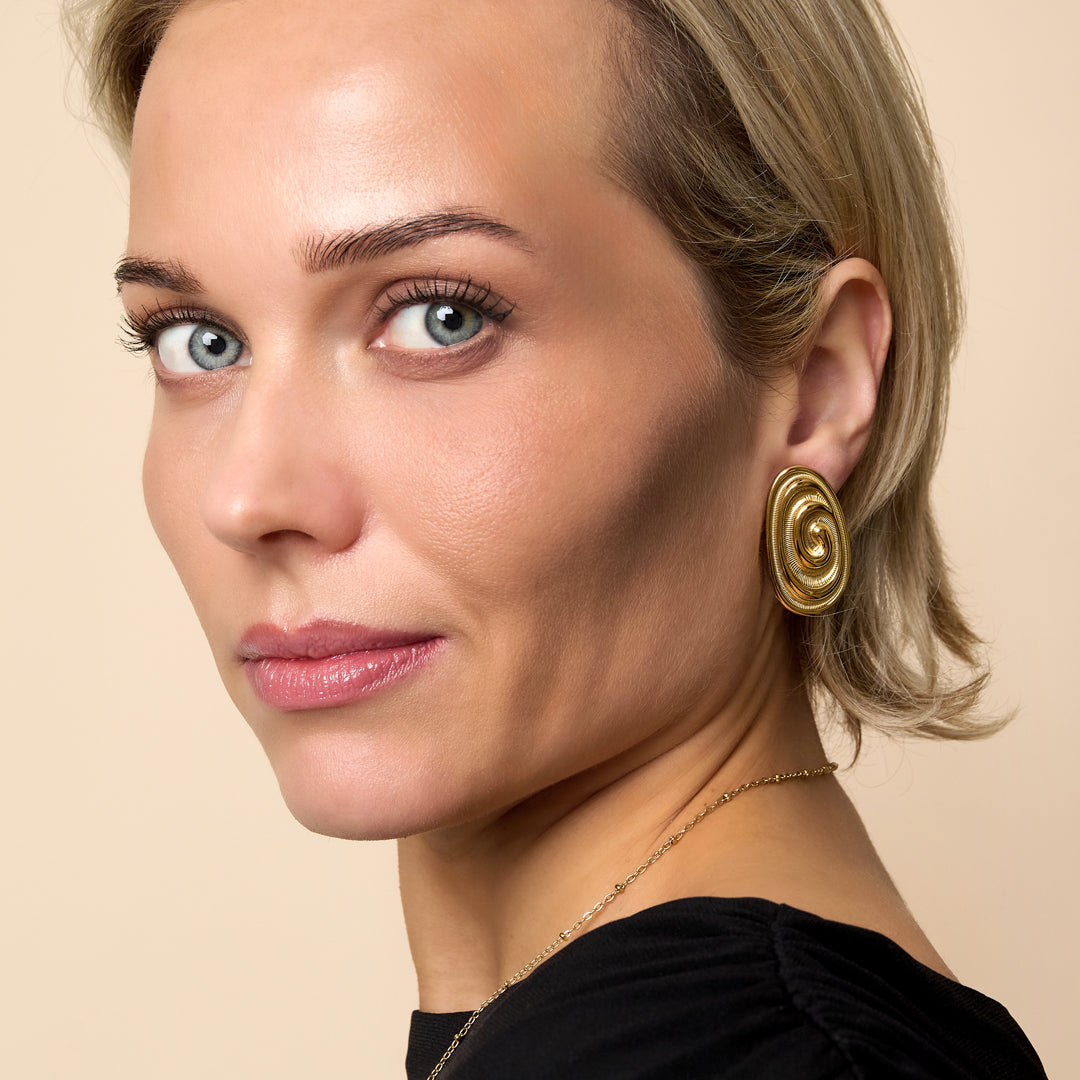 A woman wears irregular gold stud earrings and a gold necklace.
