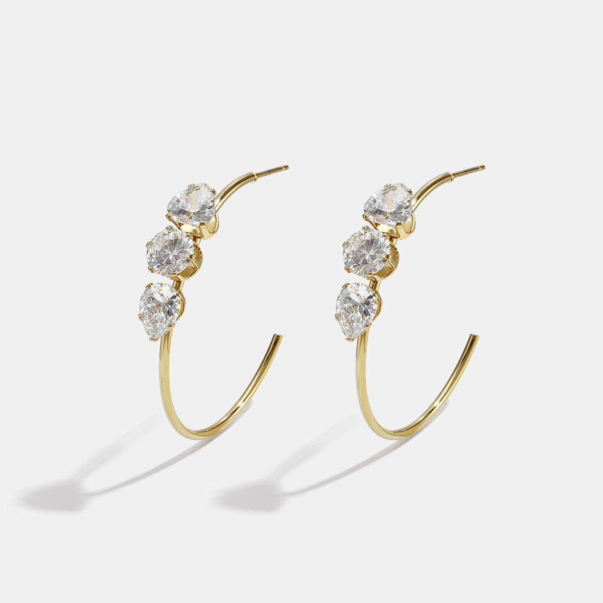 Gold hoop earrings with three clear stones each, on a white background.