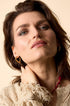 Gold heart hoop earrings worn by a woman with brown hair and blue eyes, wearing a cream textured sweater.
