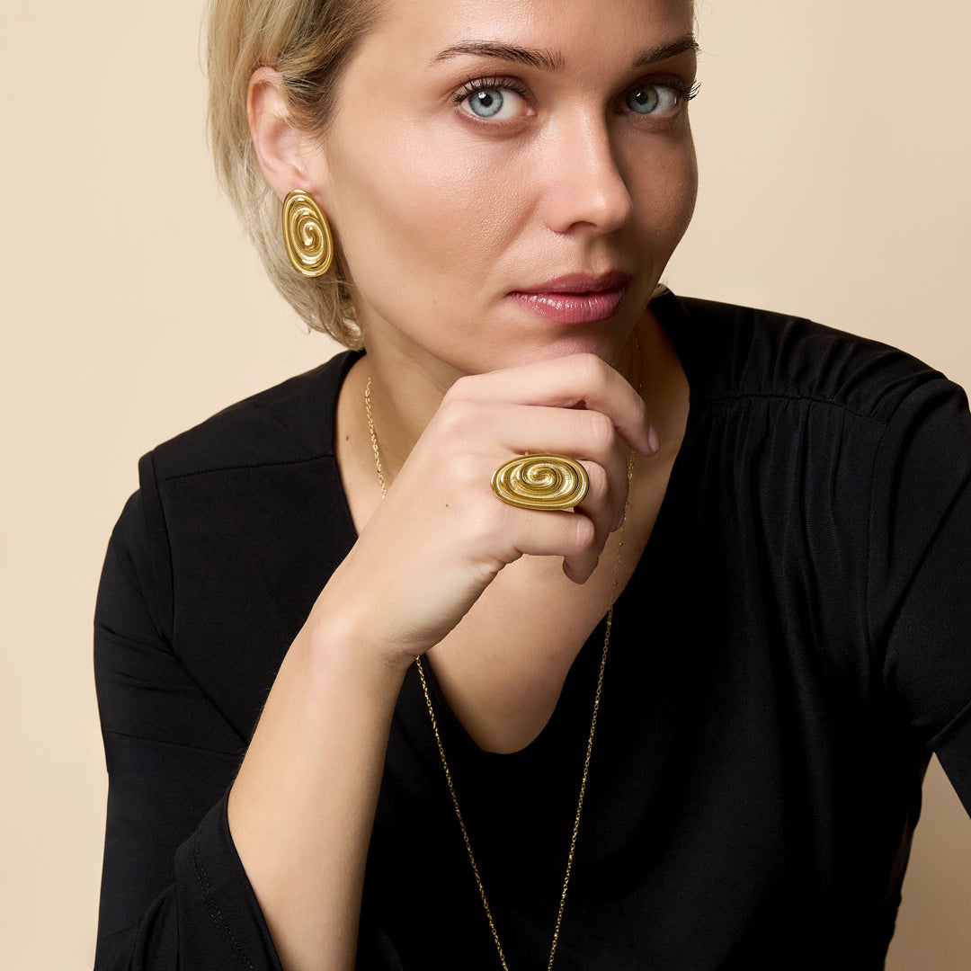 Gold irregular spiral ring on a woman's finger, with matching earrings and necklace.