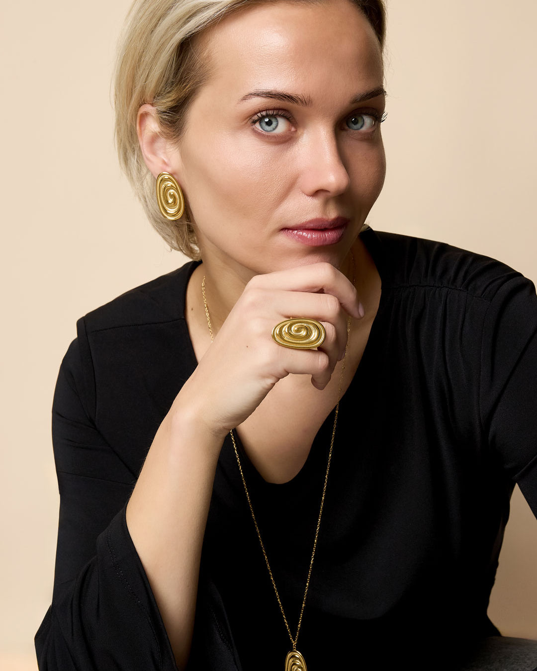 Gold irregular spiral ring on a woman's finger, with matching earrings and necklace.